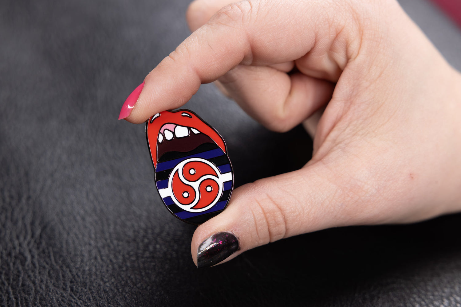 Hand holding the BDSM Pride Flag pin against a dark textured background.